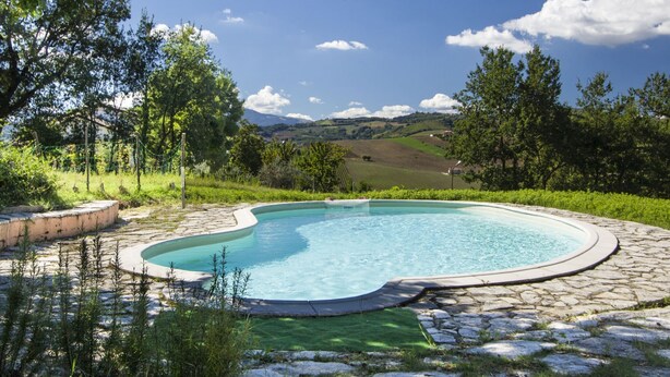 Piscina com borda de pedra e vista para o campo.