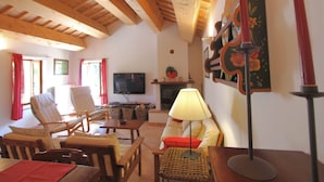 Uma sala de estar acolhedora com vigas de madeira, televisão, móveis de vime e lareira.
