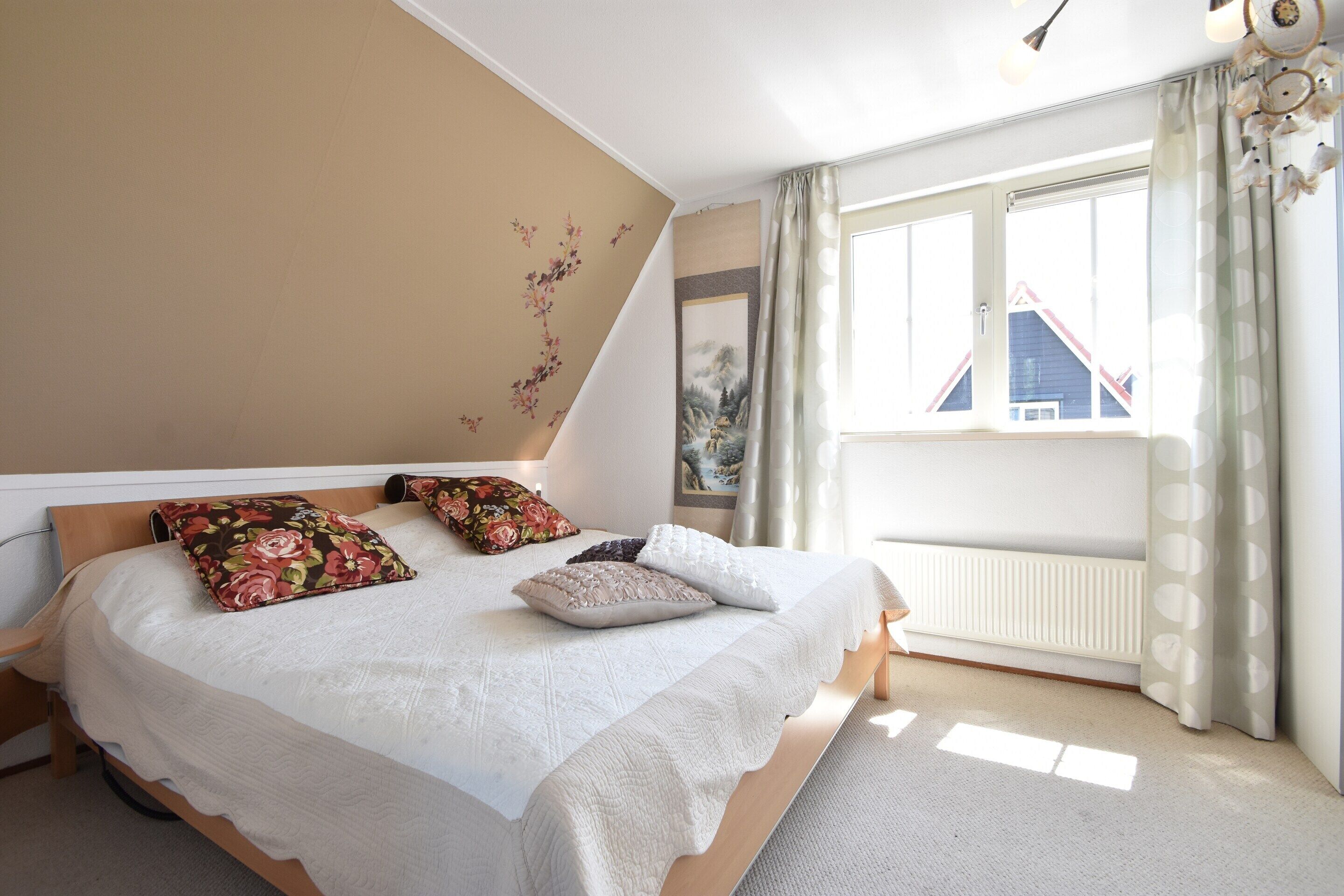 A bedroom with a large bed, a window with curtains, and a view of a house outside.