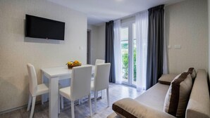 A modern living room with a flat-screen TV, a dining table with chairs, a sofa, and a view of greenery outside. - Mobile Home Banjole Near the Beach (Medulin)