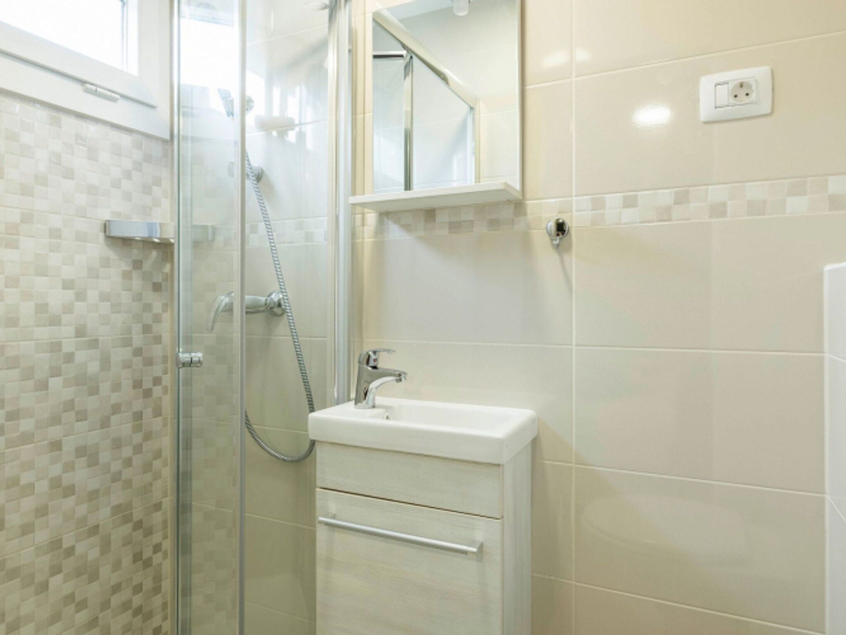 Une salle de bain avec une douche à parois de verre, un lavabo blanc et un miroir au-dessus du lavabo.