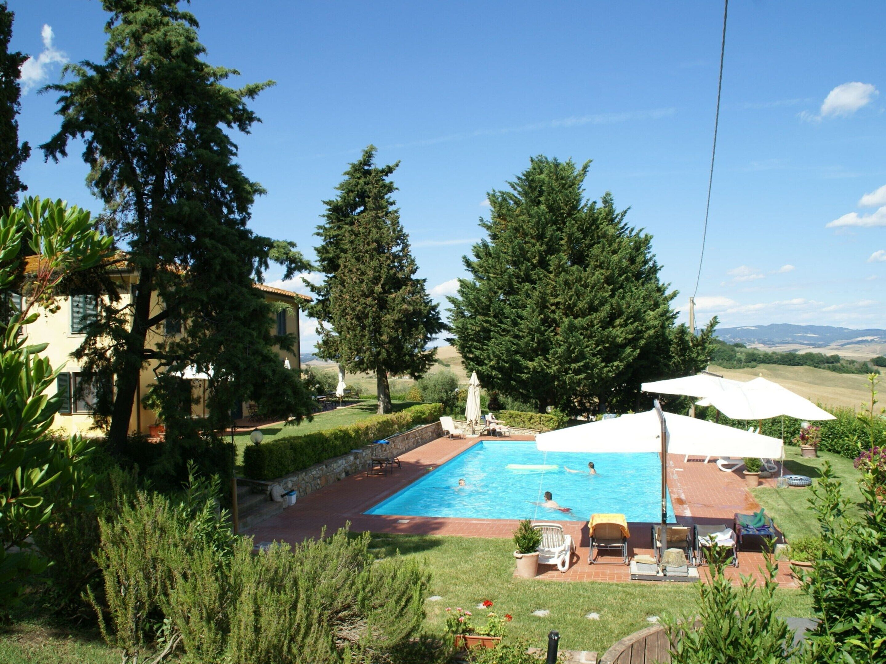 A backyard with a swimming pool, surrounded by trees and a house.
