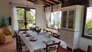 A dining area with a long table set for six, surrounded by wooden chairs. There is a white cabinet with glass doors to the right, and a television is mounted on the wall to the left. - Serene Apartment in Orciatico (Lajatico)