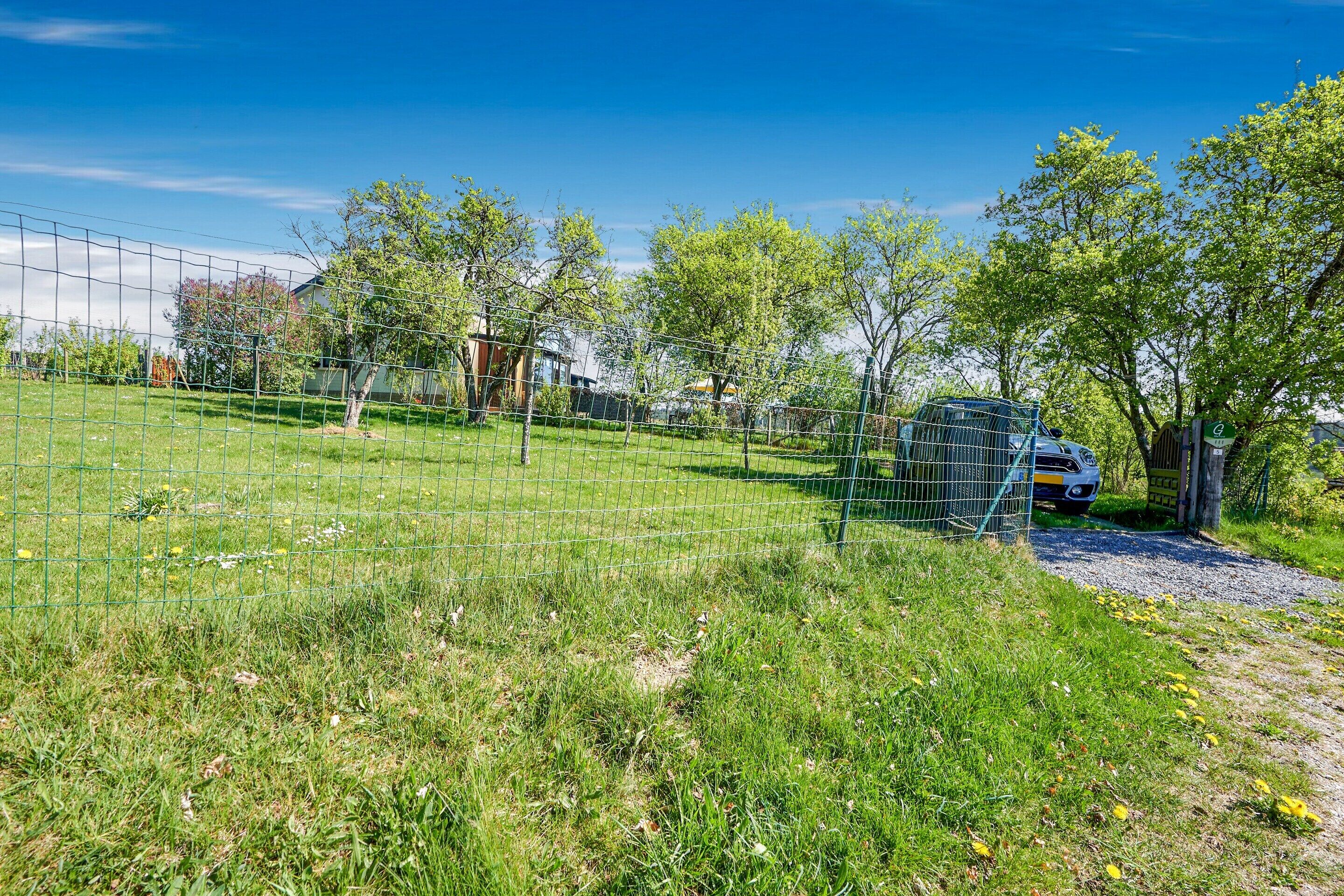 A fenced outdoor area with a gravel path, trees, and a parked vehicle.