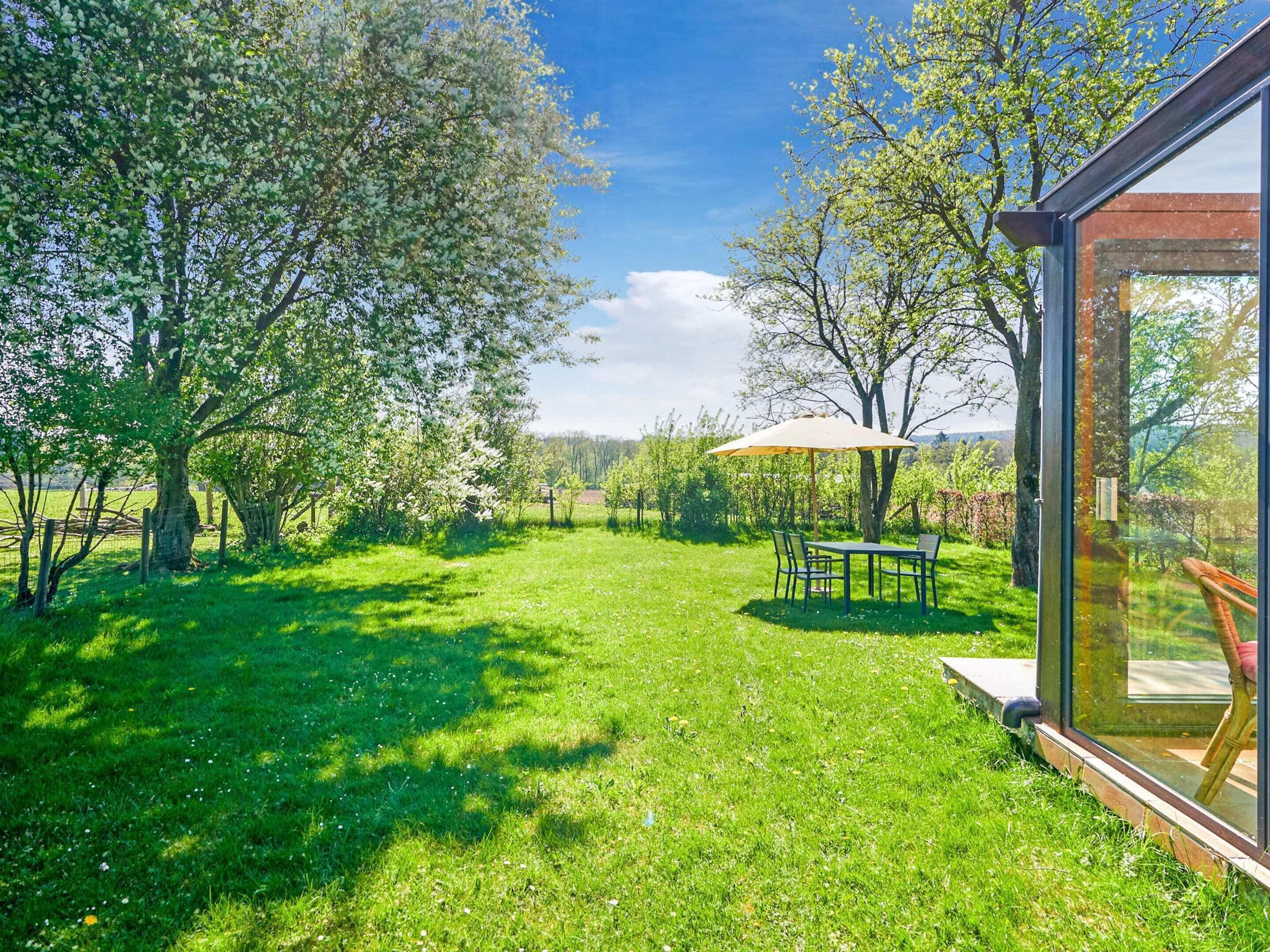 Ein sonniger Außenbereich mit Glasveranda, Tisch und Stühlen sowie einem großen Sonnenschirm.