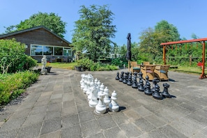 A chessboard set up on a paved patio with a wooden house in the background.