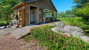 A wooden cabin with a porch, a stone sculpture, and a swing set in a garden. - Enticing Holiday Home in Eastermar near Burgumer Mar Lake (Eastermar)