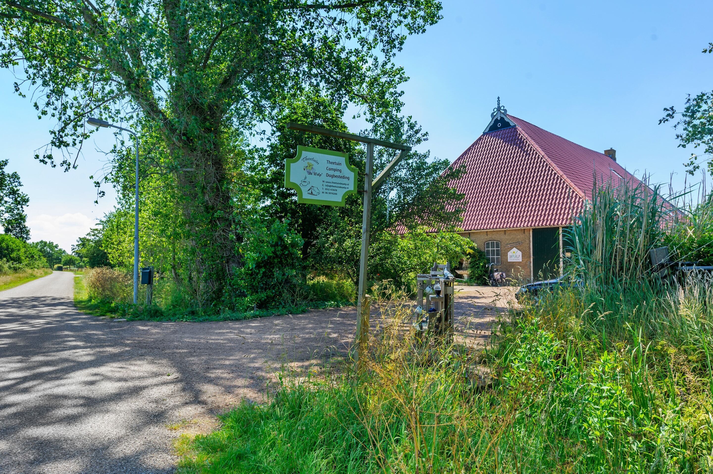 A rural setting with a sign for a camping site, a dirt road, and a building with a red roof.