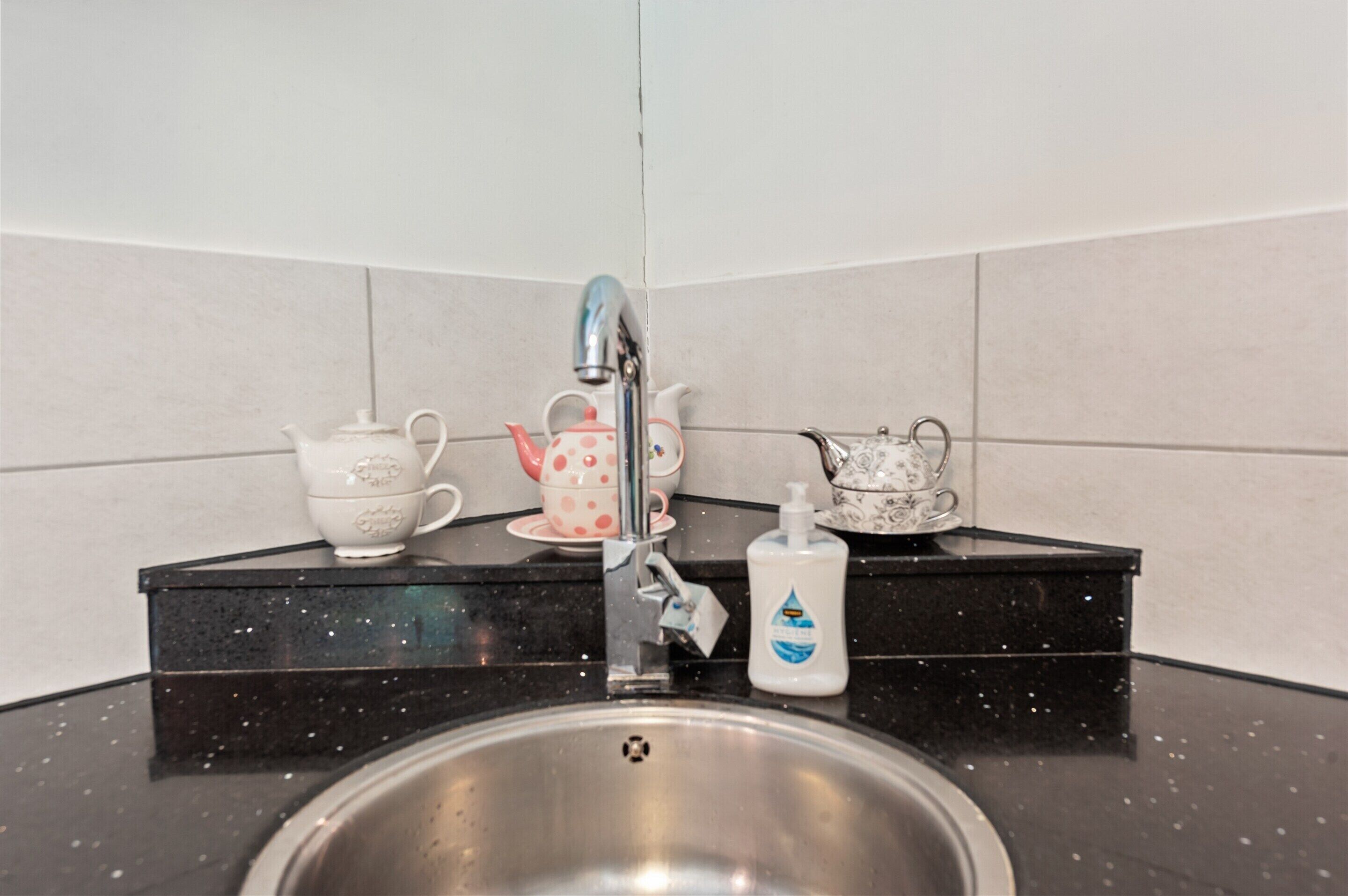 A kitchen sink with a faucet, a soap dispenser, and two teapots on a black countertop.