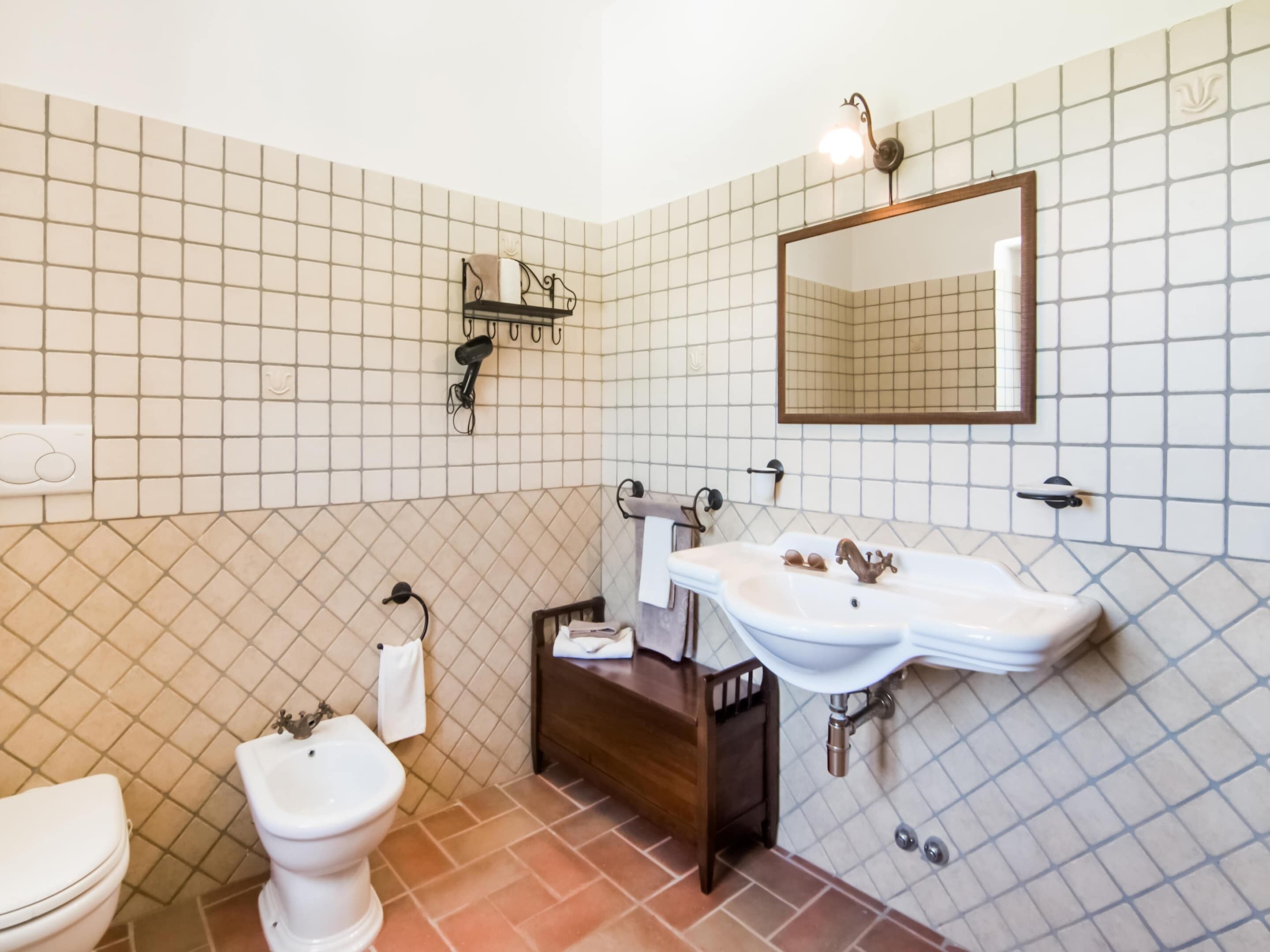 Une salle de bain équipée de toilettes, d’un bidet et d’un lavabo double, avec un miroir au-dessus.
