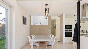 A modern kitchen with white cabinets, a dining table with chairs, and a hanging light fixture.