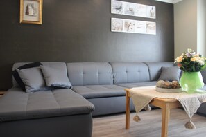 A modern living room with a grey sectional sofa, a wooden coffee table with a vase of flowers, and framed artwork on the wall. - Spacious Holiday Home in Heers near Tongeren & Sint Truiden (Heers)