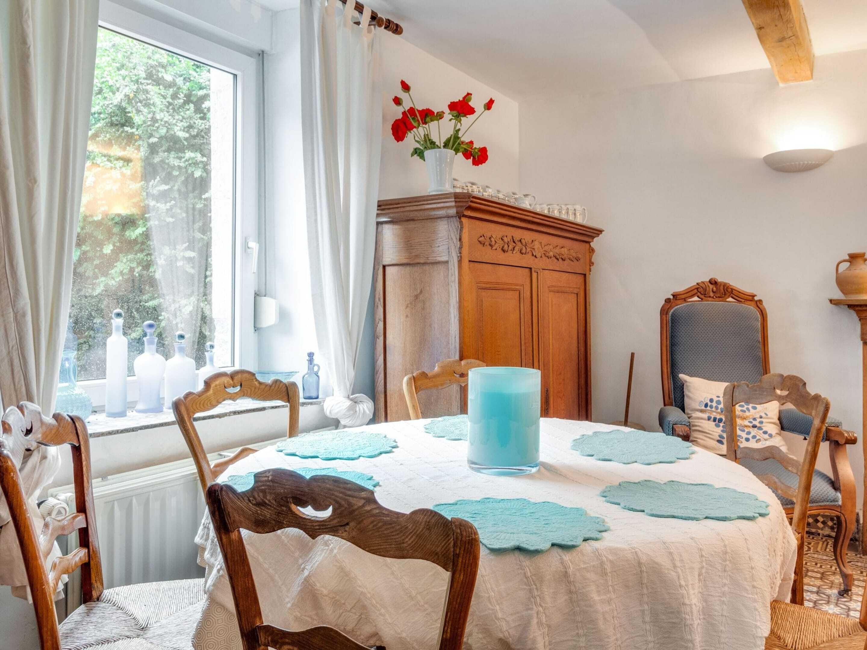 A dining room with a round table, chairs, a vase with flowers, and a wooden cabinet.