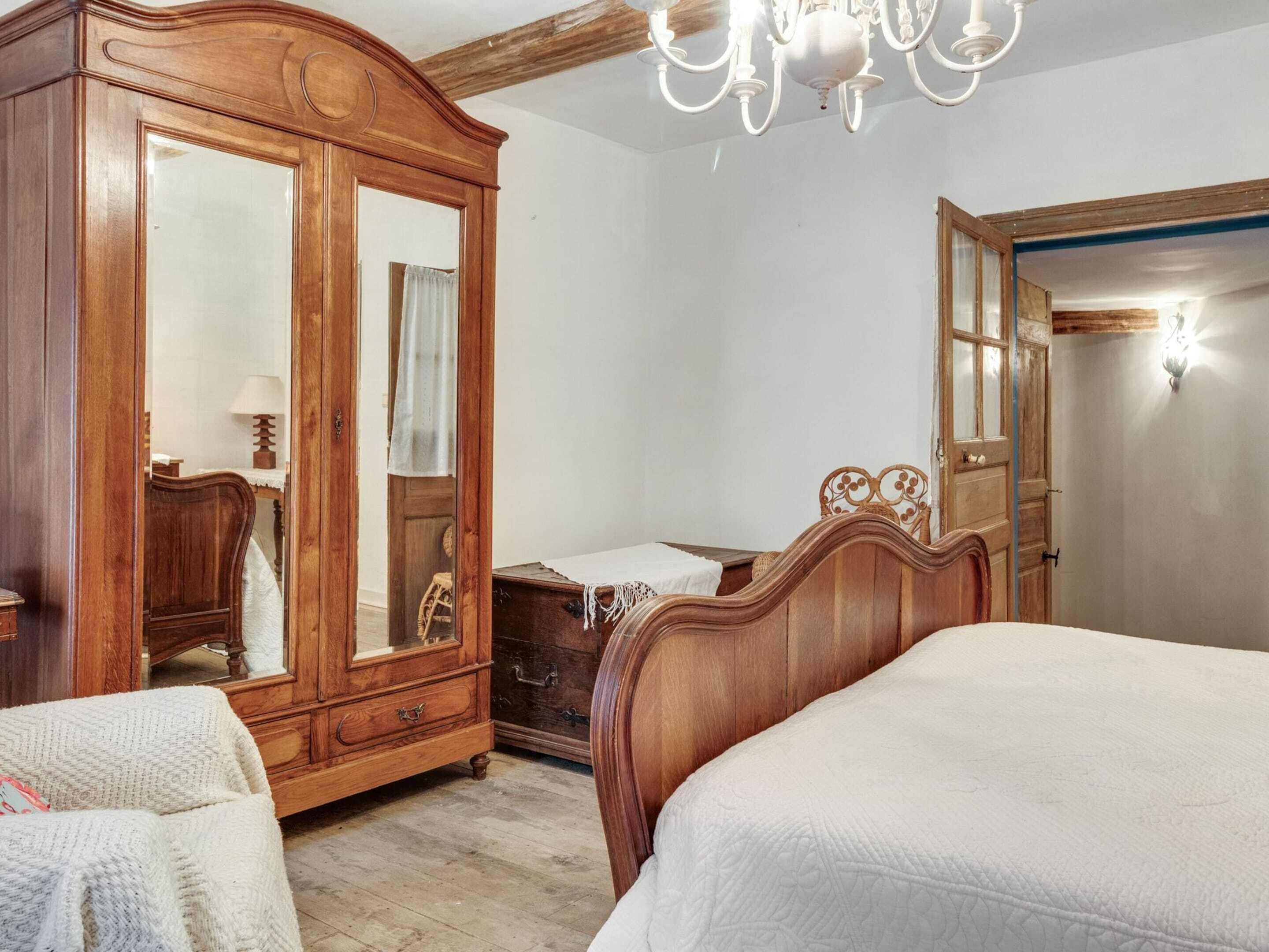 A bedroom with a wooden wardrobe, a bed, a dresser, and a chandelier.
