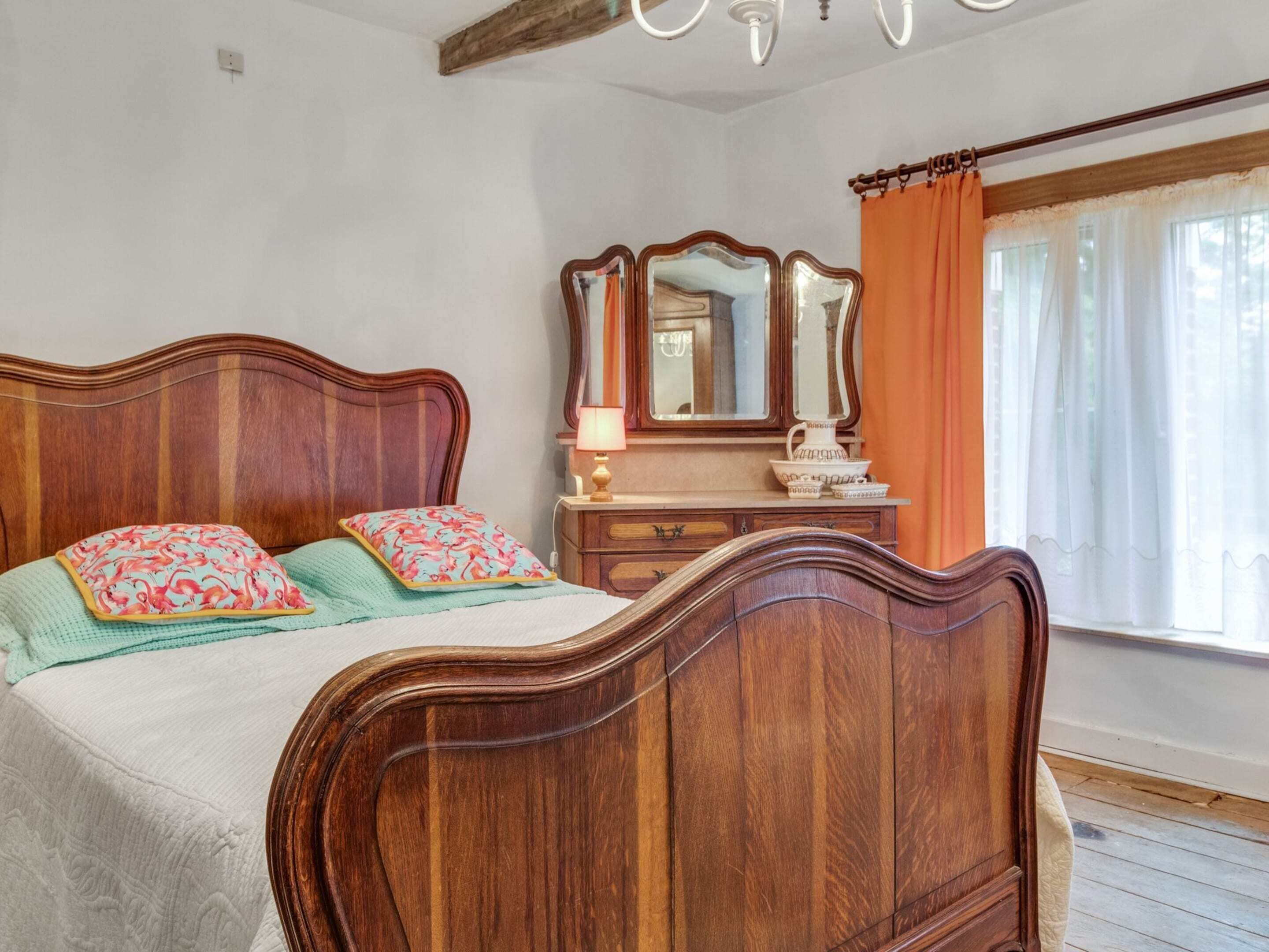 A bedroom with a wooden bed, a dresser, a mirror, and a window with curtains.