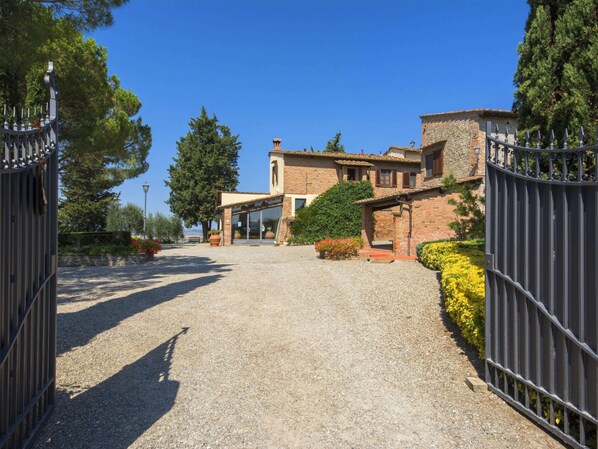 A gravel driveway leading to a building with a stone facade, a covered entrance, and a metal gate. - Belvilla by OYO Piniolmo (Castelfiorentino)