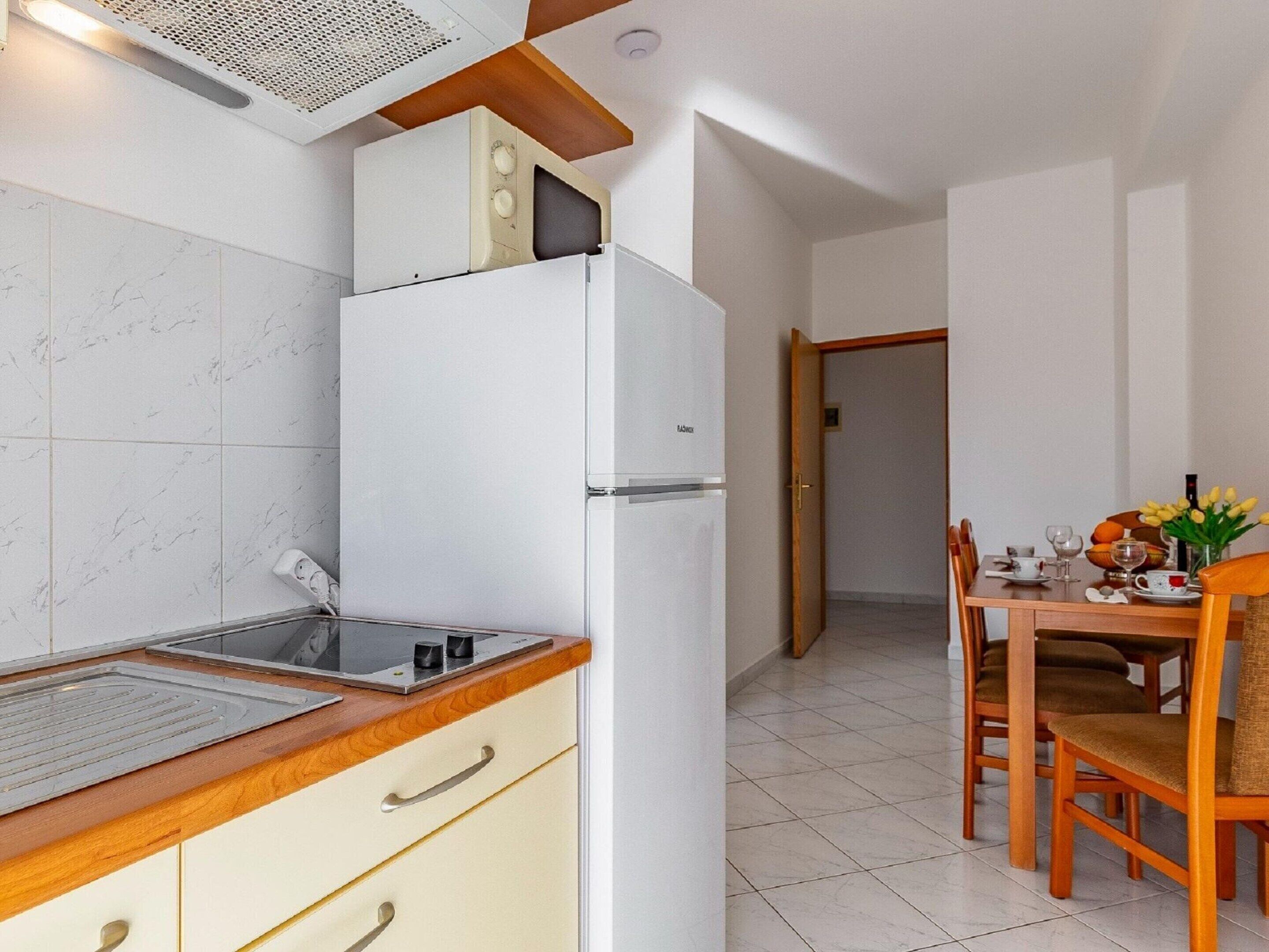 A compact kitchen with a refrigerator, a sink, and a wooden countertop. There is a dining area with a table and chairs.