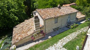 Um edifício de pedra com telhado de telhas, rodeado por vegetação e montanhas.