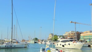 Marina com vários barcos atracados, uma grua e edifícios ao fundo.