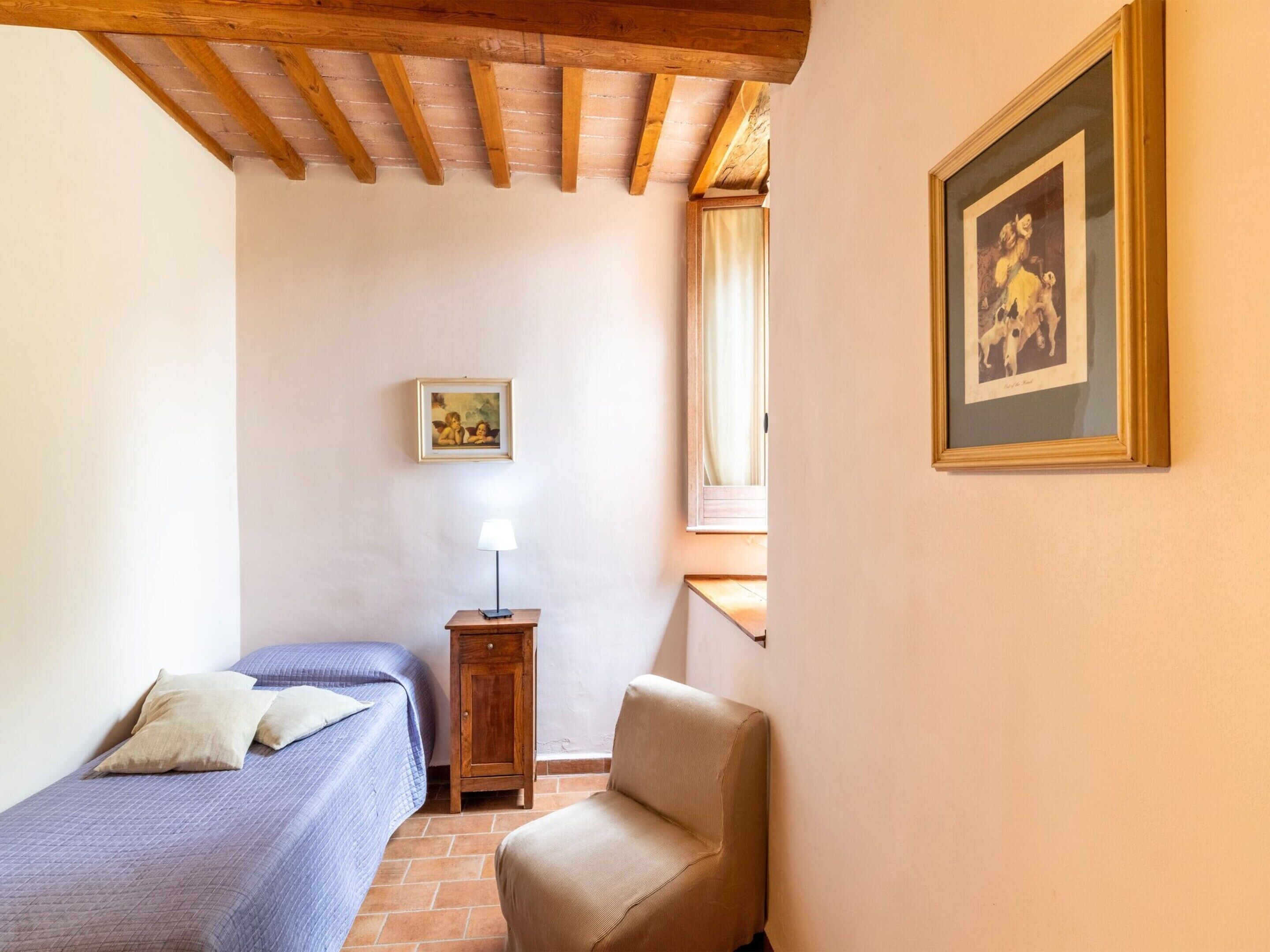 Une chambre avec deux lits simples, une armoire en bois, une chaise, une lampe et un tableau encadré au mur.
