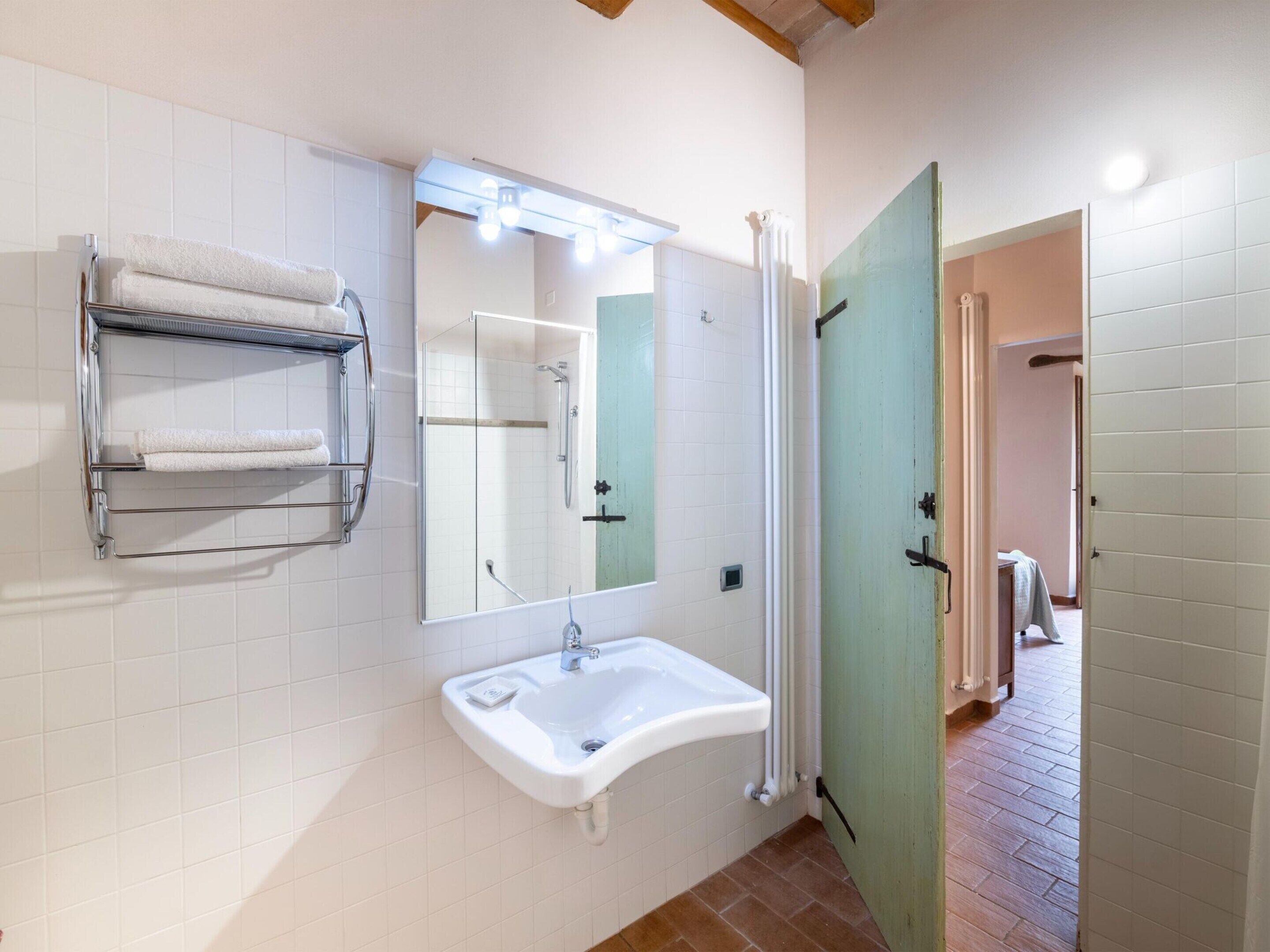 Baño con lavamanos, espejo, toallero y ducha.
