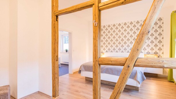 A room with a wooden truss ceiling, a bed with a patterned headboard, and a view of another room through an open doorway. - Holiday Home With Private Terrace (Clausthal-Zellerfeld)