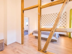 A room with a wooden truss ceiling, a bed with a patterned headboard, and a view of another room through an open doorway. - Holiday Home With Private Terrace (Clausthal-Zellerfeld)