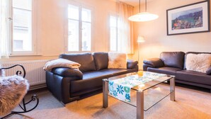A cozy living room with a dark leather sofa, a glass coffee table, and a fluffy armchair. - Holiday Home With Private Terrace (Clausthal-Zellerfeld)