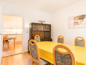 A dining area with a yellow table, four chairs, a cabinet with glass doors, and a wall-mounted clock. - Holiday Home With Private Terrace (Clausthal-Zellerfeld)