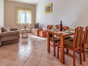 A living room with a sofa, a TV, a dining table with chairs, and a window with curtains. - Lovely Apartment in Banjole near Beach & Town Center (Medulin)