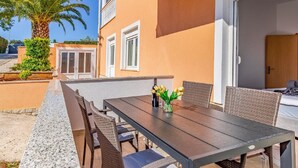 An outdoor patio with a dining table and chairs, a palm tree, and a building with a balcony. - Lovely Apartment in Banjole near Beach & Town Center (Medulin)
