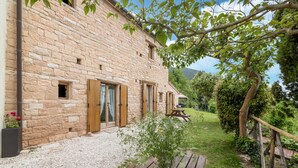 Un bâtiment en pierre avec des volets en bois, un chemin de gravier et un banc en bois.