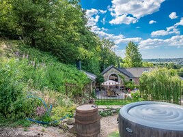 A rustic outdoor seating area with stone walls, a stone roof, and a view of a village in the distance.