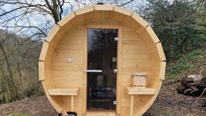 Un sauna en bois de forme circulaire, doté d’une porte et d’un petit banc à l’extérieur.