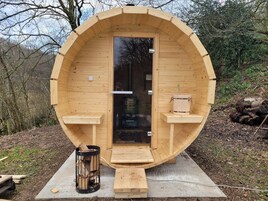 Una sauna de madera con diseño circular, una puerta y un pequeño banco en el exterior.