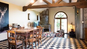 Un coin repas avec un sol à carreaux, des meubles en bois, une cheminée en pierre et une grande fenêtre.