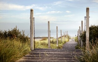 Una pasarela de madera que conduce a una playa, con postes y cadenas de madera.