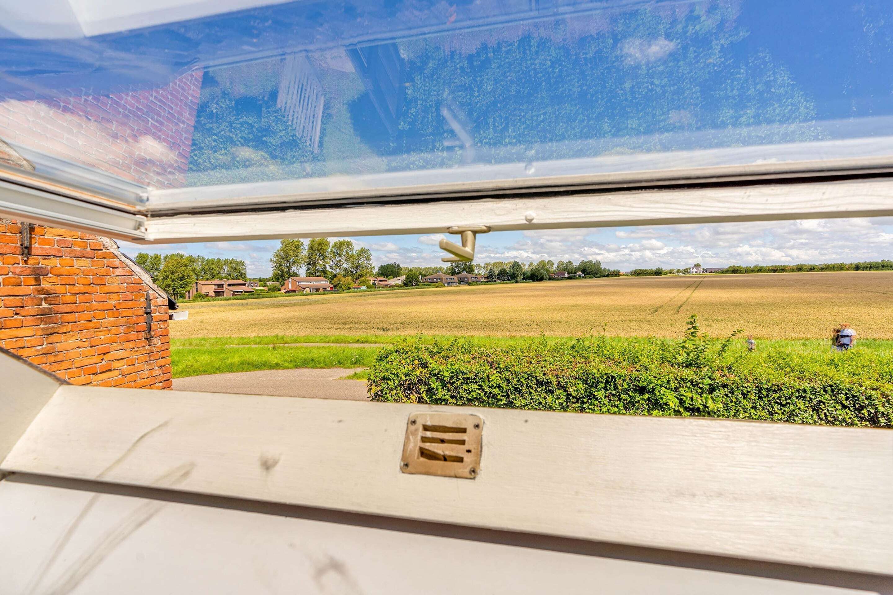 A window with a view of a field, a brick wall, and a metal structure.