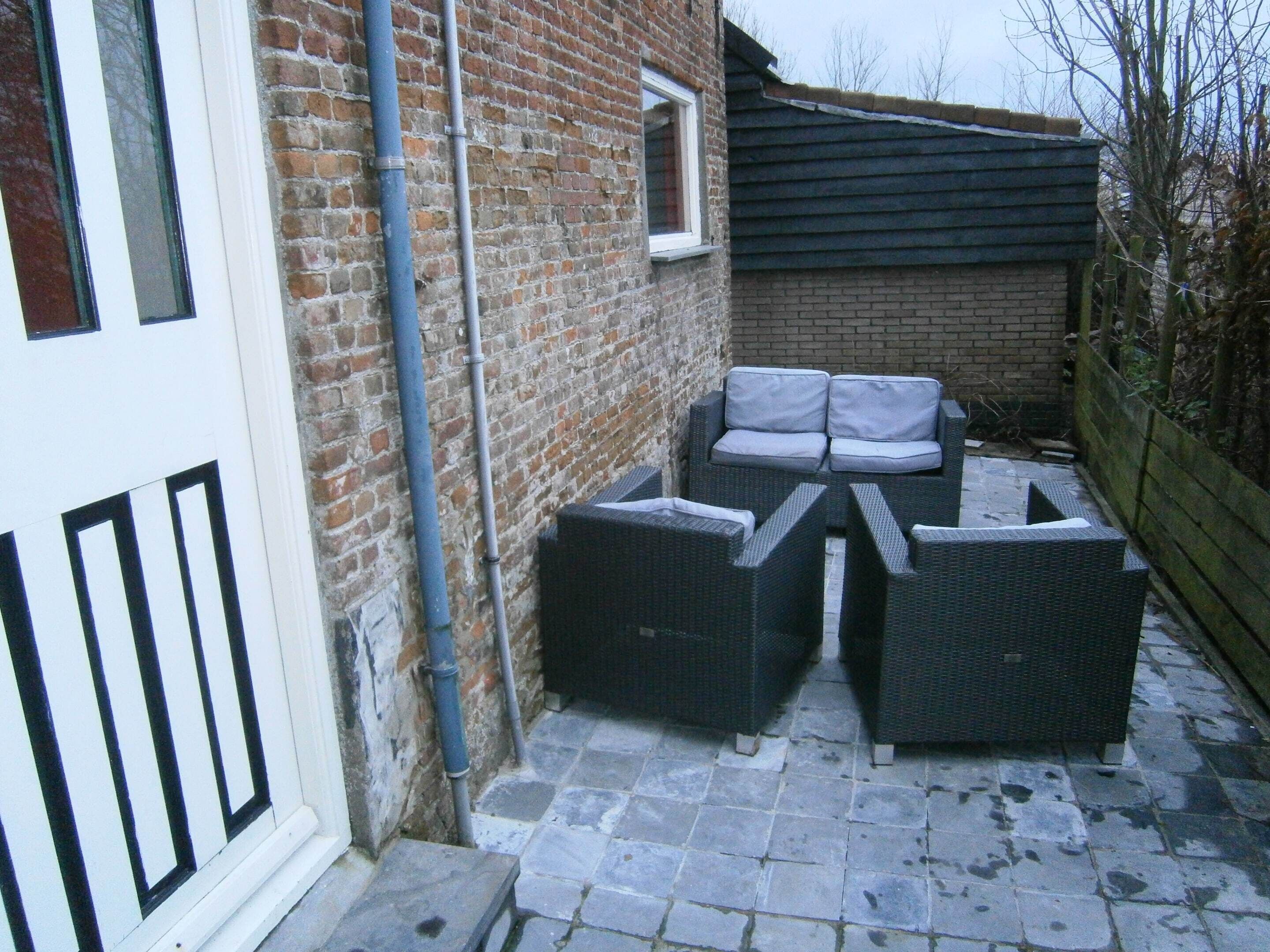 A courtyard with a brick wall, a white door, and outdoor furniture.