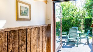 A room with a wooden bench, a framed picture on the wall, and a view of an outdoor patio with chairs and greenery.