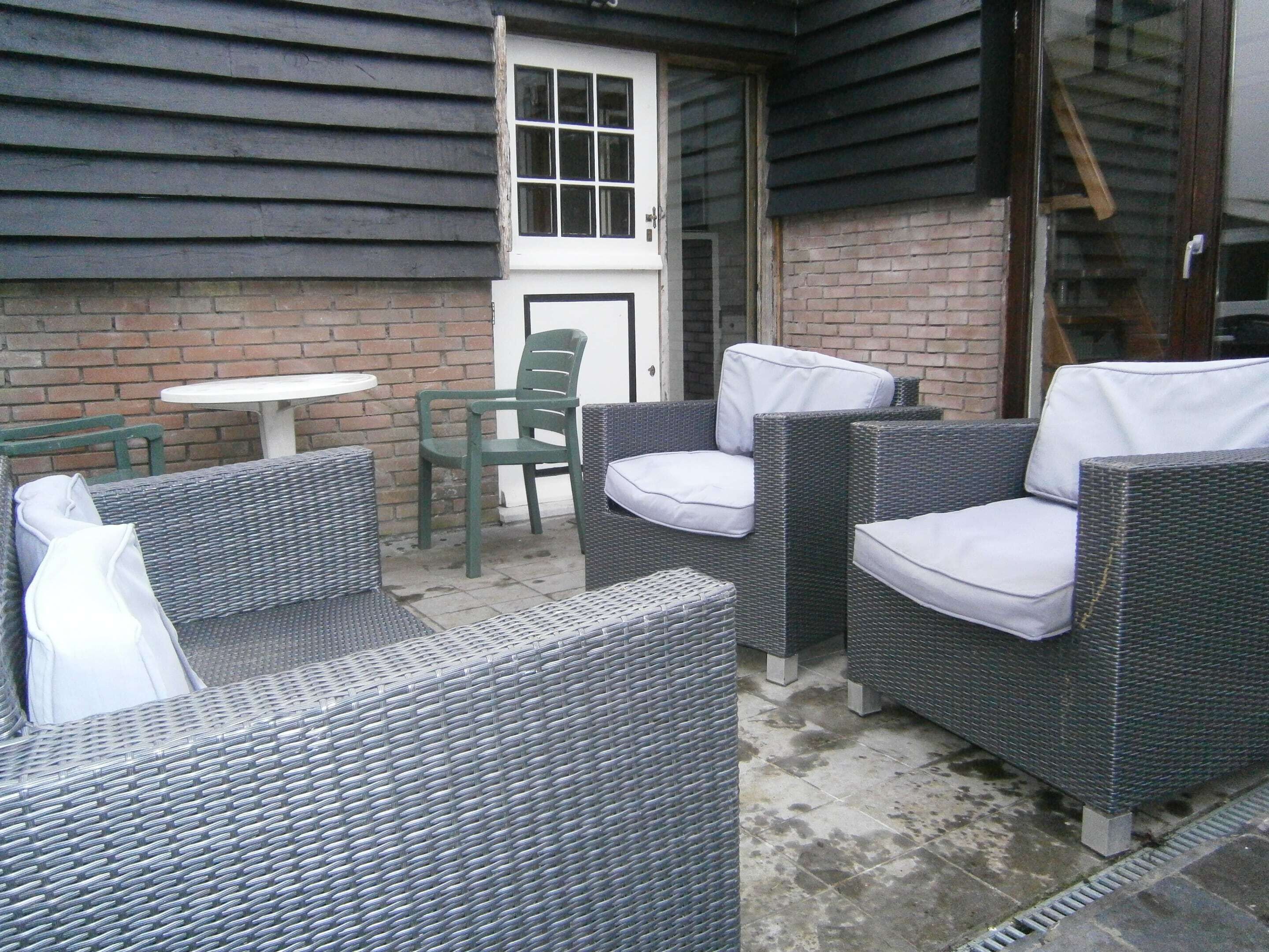 A patio area with wicker furniture, a small round table, and a door leading to a brick wall.