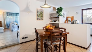 Ein Essbereich mit Holztisch und -stühlen, einer Pendelleuchte und einer Küchenzeile inklusive Kaffeemaschine und Toaster.