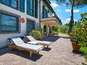 Uma villa com duas poltronas na área externa, um pátio com piso de pedra e vista para o verde ao redor.