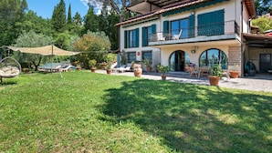 Ein zweistöckiges Haus mit Balkon, Garten und Sitzgelegenheiten im Freien.