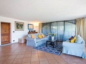 Uma sala de estar com um sofá listrado, um sofá azul e branco, uma pequena mesa com um vaso de flores e uma porta de madeira.