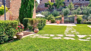A courtyard with a brick wall, a tall cypress tree, and a stone pathway leading to a gate. - Belvilla by OYO Il Melograno (Montalcino)