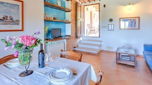 A dining area with a table set for two, a television on a shelf, and a view of the outside through an open door. - Belvilla by OYO Il Melograno (Montalcino)