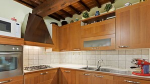 Una cocina con armarios de madera, estufa a gas, microondas y una cafetera roja.