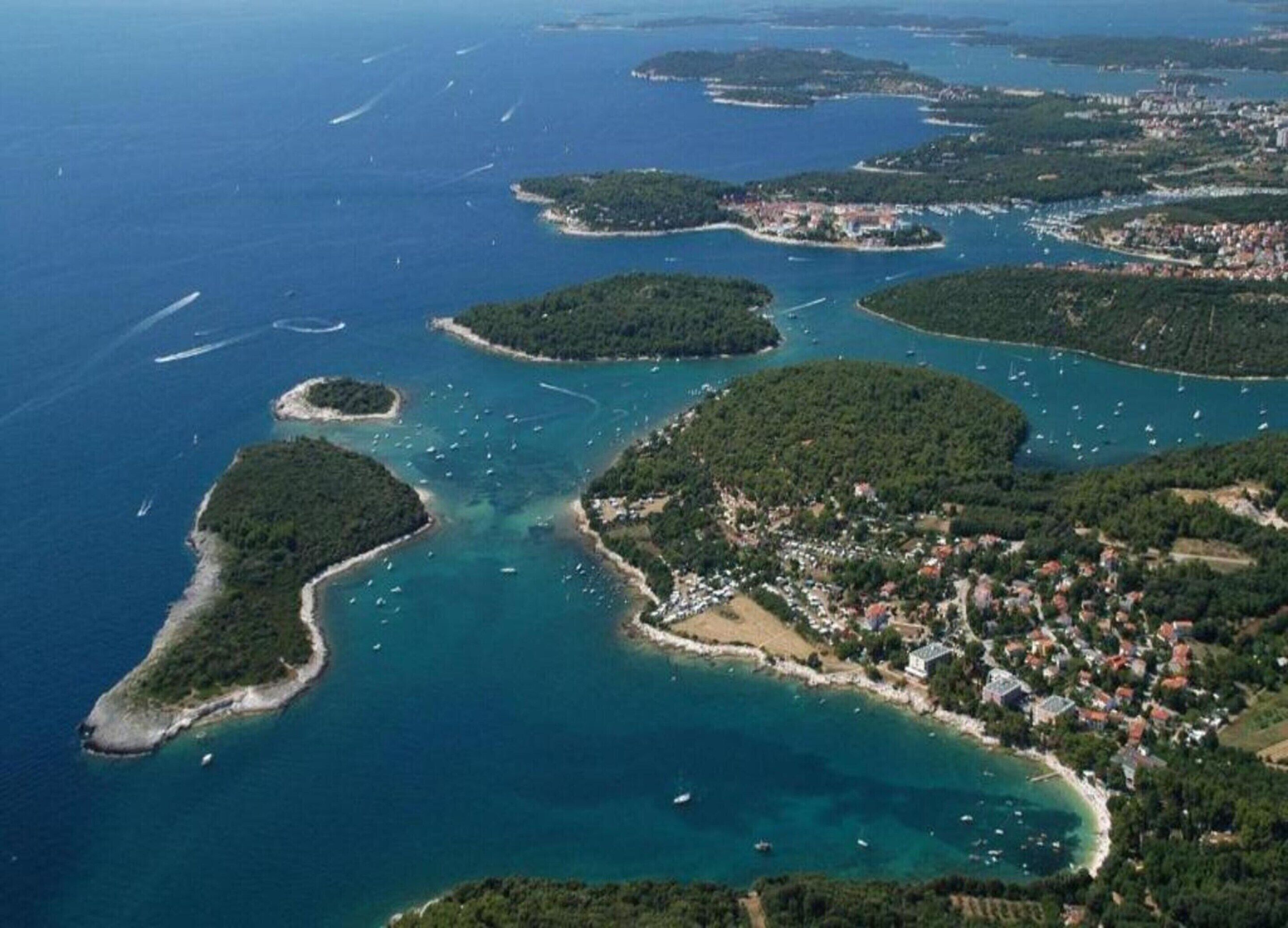 Eine Vogelperspektive zeigt eine Küstenregion mit mehreren Inseln, klarem, blauem Wasser und einer dicht besiedelten Stadt mit Gebäuden und Grünflächen.
