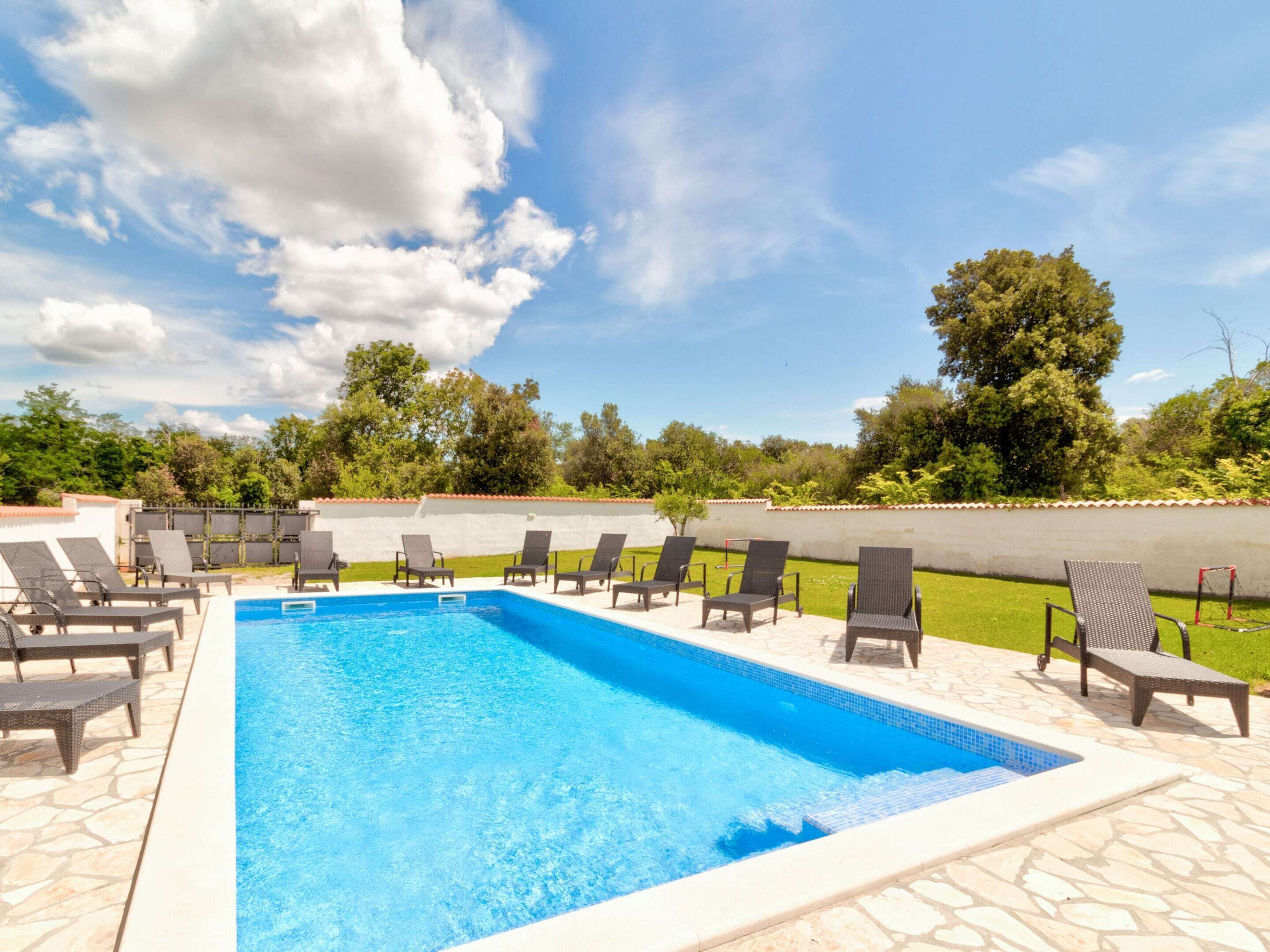 Una piscina rettangolare con acqua cristallina e azzurra, circondata da piastrelle di pietra.